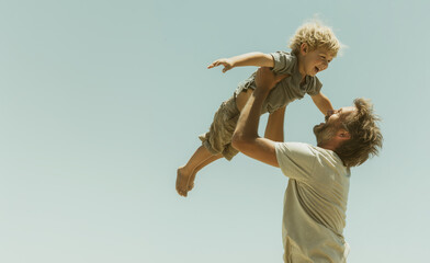 Father lifting happy son playing airplane against sky