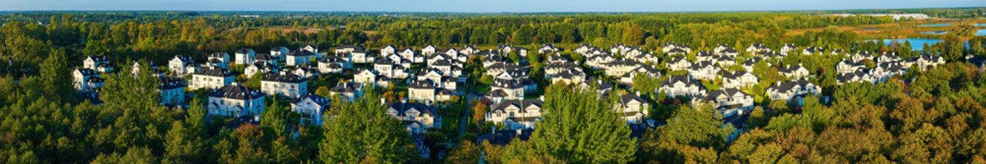 Modern housing estates blended into the autumn landscape with yellow trees on a bright day, panoramic view.
