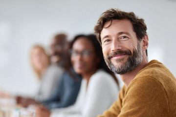 Confident, smiling man with diverse colleagues in background. Represents leadership, teamwork, inclusivity,  success. Perfect for corporate, business, and diversity themes.