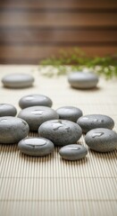 Smooth gray spa stones with water droplets on a bamboo mat with green leaves and wooden background massage stones
