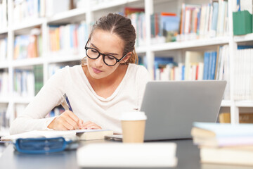 Young female university student studying at a desk in the college library