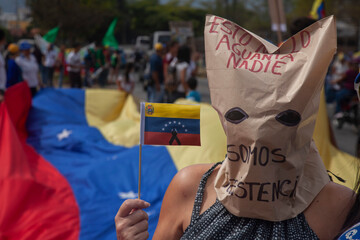 Protester wearing a mask and carrying a Venezuelan flag during a citizen protest.