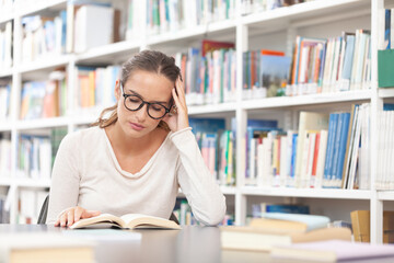 Young female student is concentrated on reading a book sitting at a desk in the library