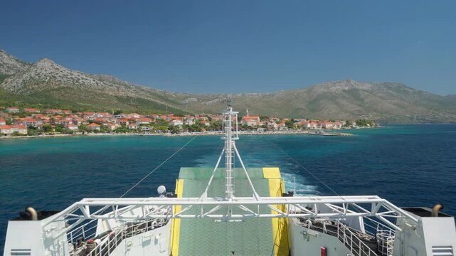 View from the stern of a car ferry leaving the port of Orebic in Dalmatia. Ship's wake on the blue sea with the Peljesac peninsula coastline in the background.