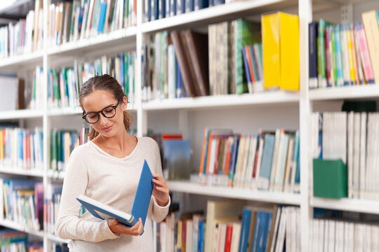 Fototapeta Young woman reading a book in a modern library