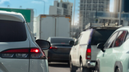 Fototapeta premium Rear side of luxury white car and turn on brake light. Traffic jam on the road in the city. Blurred background of cars and cities and tall buildings under blue sky.