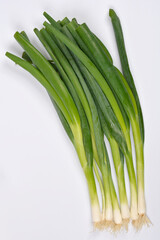 A fresh bunch of green spring onions with white bulbs and roots is diagonally arranged on a plain white studio background
