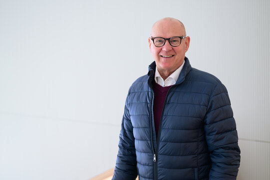 Portrait of a happy senior man smiling at the camera while standing indoors wearing blue jacket