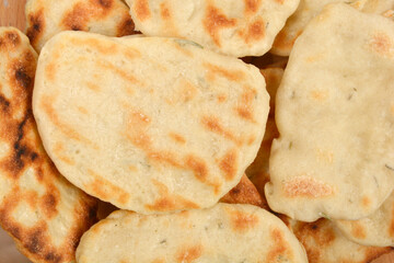 A close-up shot of a pile of small, round flatbreads with golden-brown grill marks, suggesting they were cooked on a skillet