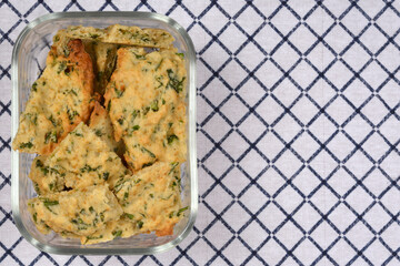 An overhead shot shows a glass container filled with homemade savory crackers with parsley, set against a blue and white checkered cloth