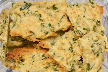 A close-up, overhead view of a glass container filled with a pile of homemade savory crackers seasoned with parsley