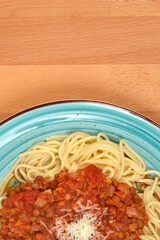 An overhead shot of a plate of spaghetti topped with vegan lentil Bolognese sauce and grated cheese, set on a blue dish over a wooden table