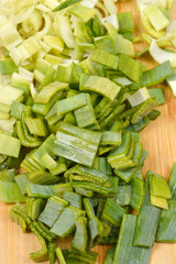 A close-up shot captures the texture of a pile of freshly chopped leeks showing a vibrant green-to-pale-yellow gradient on a wooden cutting board