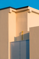 Minimalist architecture detail of modern building facade illuminated by warm sunset light, geometric shapes and clean lines against clear blue sky.