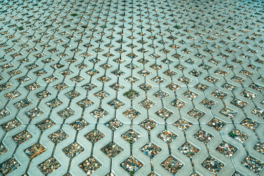 Permeable concrete pavers with gravel stones filling geometric gaps, eco-friendly pavement. Pattern of interlocking pavers with stone-filled holes, sustainable ground surface texture.