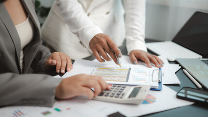 Two businesswomen analyzing financial reports and charts using calculator in modern office