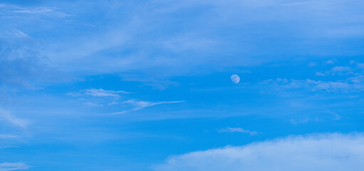 Sky and clouds with the moon visible during the day,Clear blue sky with fluffy clouds and a...