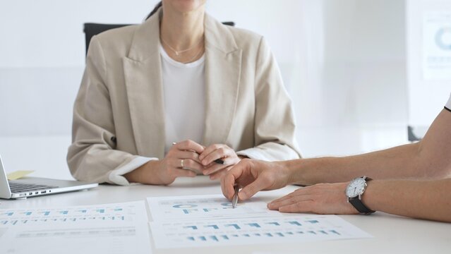 Professional businesspeople collaborating on financial analysis, female executive gesturing toward charts while presenting strategic insights to team members in corporate workspace