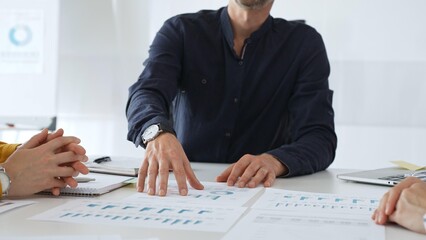 Professional colleagues reviewing financial charts, collaborating on strategic planning, gesturing toward data visualizations during corporate meeting in contemporary workspace
