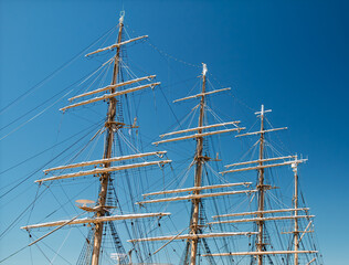 Sailing masts rise against a clear blue sky at a coastal harbor showcasing the art of traditional nautical craftsmanship