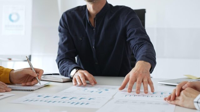 Professional colleagues reviewing financial charts, collaborating on strategic planning, gesturing toward data visualizations during corporate meeting in contemporary workspace