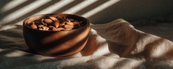 The gentle glow of warm sunlight casts a beautiful sheen over a bowl filled with almonds and walnuts. This delightful arrangement sits gracefully on a soft linen cloth, contributing to a serene and we