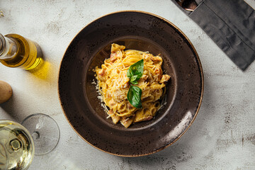 Classic Italian carbonara pasta with bacon, parmesan, and basil served in a deep dark plate