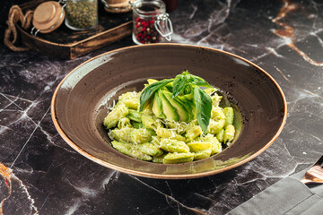 Pasta served with creamy avocado and basil pesto in a deep brown ceramic bowl on a marble table
