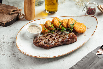 Delicious grilled beef steak served with crispy hash browns and creamy sauce on a white plate