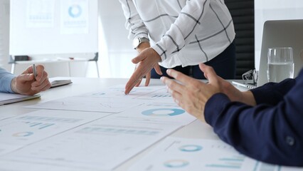 Business team analyzing financial charts and data reports during strategy meeting, hands pointing to documents on table with graphs and diagrams for planning © rogerphoto
