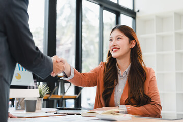 Young woman smiling and shaking hands in modern office during business meeting expressing confidence and warmth