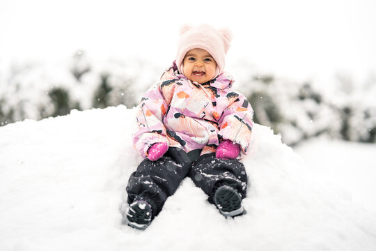 Adorable happy toddler girl between one and two years old exploring fresh snow outdoors, smiling and joyful in a warm snowsuit and winter hat.