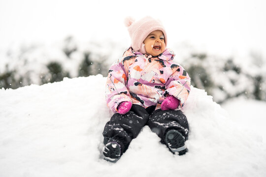 Adorable happy toddler girl between one and two years old exploring fresh snow outdoors, smiling and joyful in a warm snowsuit and winter hat.