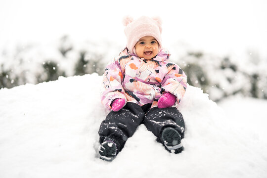 Adorable happy toddler girl between one and two years old exploring fresh snow outdoors, smiling and joyful in a warm snowsuit and winter hat.