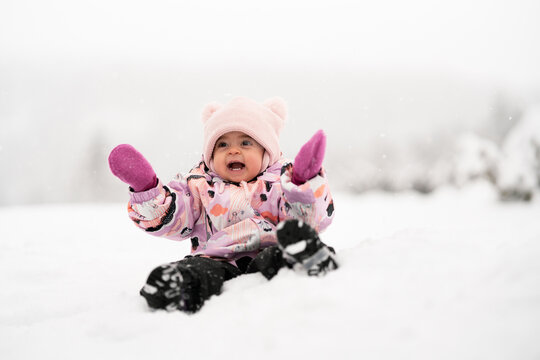 Adorable happy toddler girl between one and two years old exploring fresh snow outdoors, smiling and joyful in a warm snowsuit and winter hat.