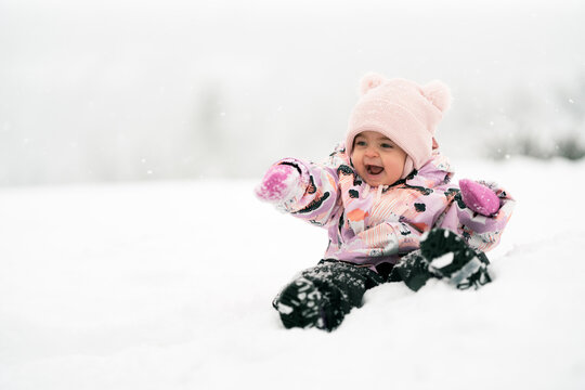 Adorable happy toddler girl between one and two years old exploring fresh snow outdoors, smiling and joyful in a warm snowsuit and winter hat.