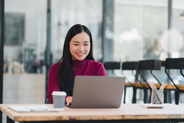 Young woman working on laptop in modern cafe, smiling while typing and enjoying coffee and creative workspace