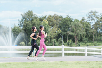 Two women jogging in activewear by lakeside with fountain and trees, energetic outdoor fitness scene