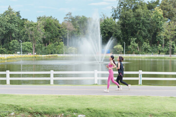 Two women jogging along lakeside path with fountain spray and green trees, energetic outdoor fitness scene