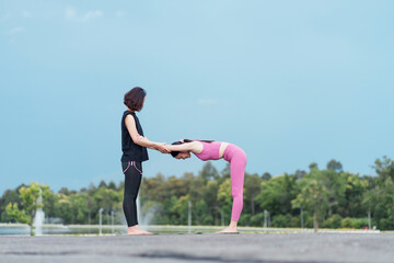 Young woman stretching with trainer outdoors in park, yoga exercise with assisted backbend, serene fitness moment