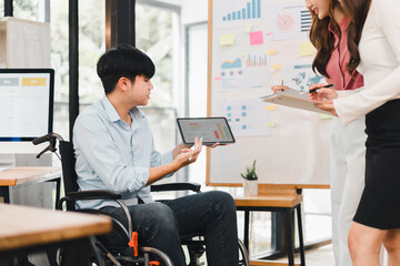 Young businessman in wheelchair presenting tablet with charts to colleagues, collaborative office meeting with charts and sticky notes