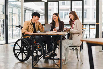 Young man in wheelchair meeting with two businesswomen, collaborative office discussion, inclusive teamwork and positive atmosphere