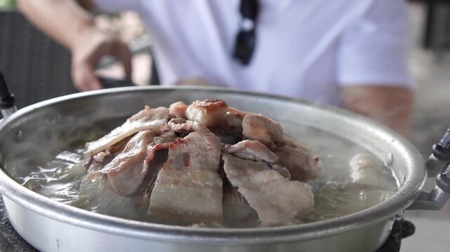 Delicious pork slices grilling over hot coals on a traditional Thai Moo Krata setup. Smoke and steam rise from the cooking process, creating an appetizing and dynamic scene. Slow motion.