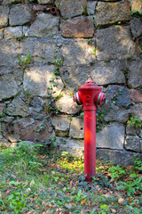 Bright red fire hydrant stands against a weathered stone wall in a serene outdoor setting
