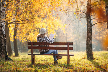 Woman reading book in autumn park. Digital detox, mental wellbeing and relaxation on fresh air outdoors