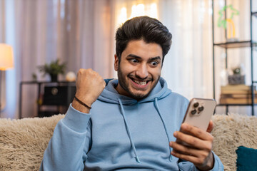 Surprised excited Indian young man holding smartphone, amazed by online game win or good news....