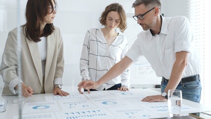 Professional team analyzing financial data, corporate colleagues carefully examining charts and graphs in modern workplace. Business people concept