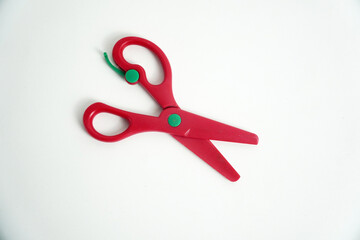 A pair of red plastic safety scissors with green pivot points, lying open on a clean white background. safe scissors for children learning to cut. school, crafts, art projects, and office supplies.