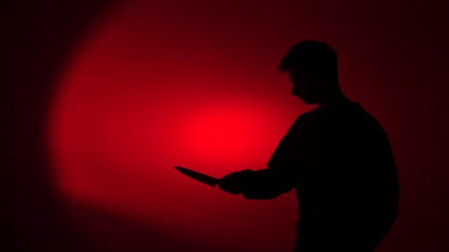 Silhouette man holding knife in red light