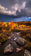 Obraz premium Vibrant autumnal scene featuring a flowing stream, foliage, and dramatic sky